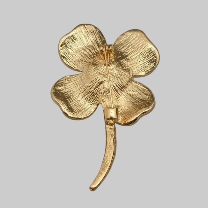 Backside of four-leaf clover brooch with green leaves and a gold center on a light gray background