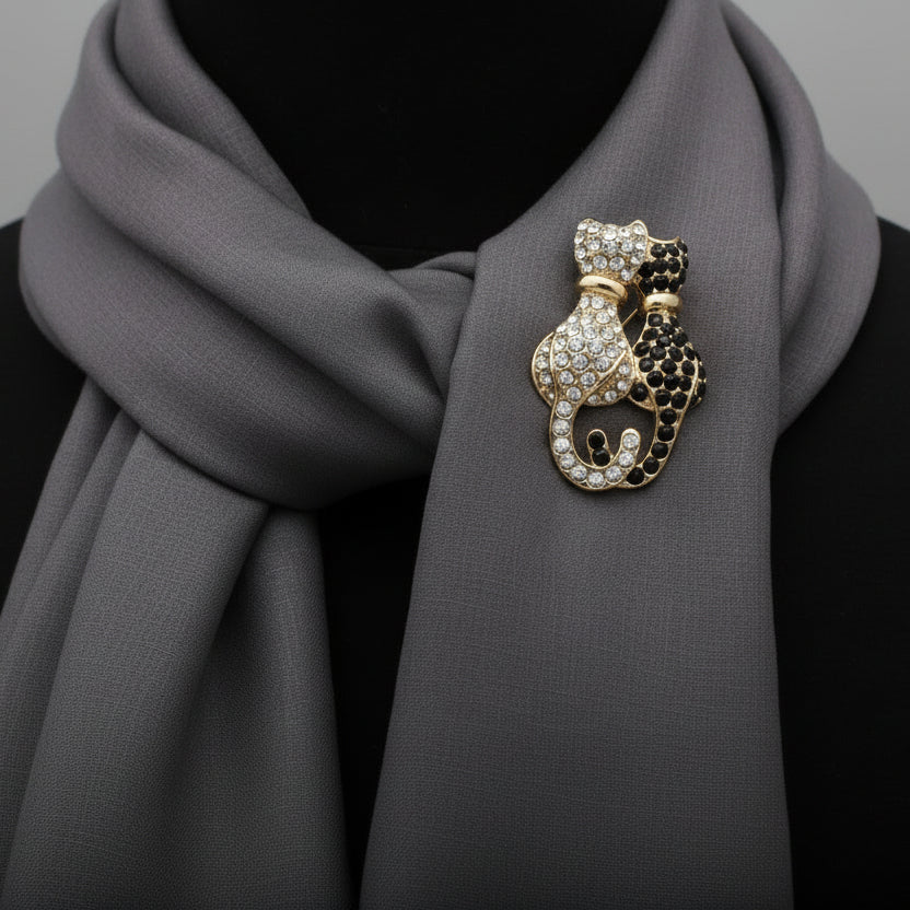 Black and white rhinestone double cat shaped brooch pinned to a soft gray scarf against a black top