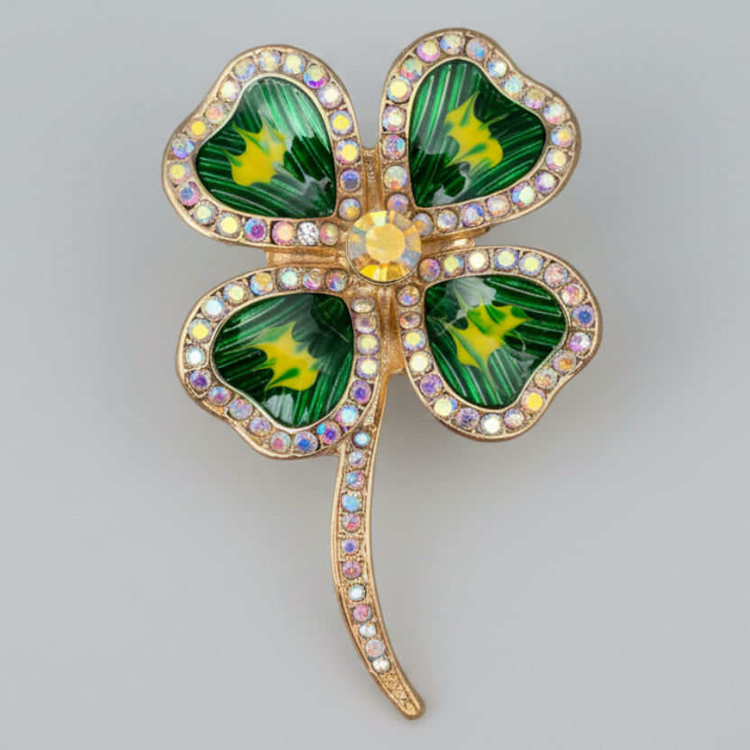 Four-leaf clover brooch with green leaves and a gold center on a light gray background