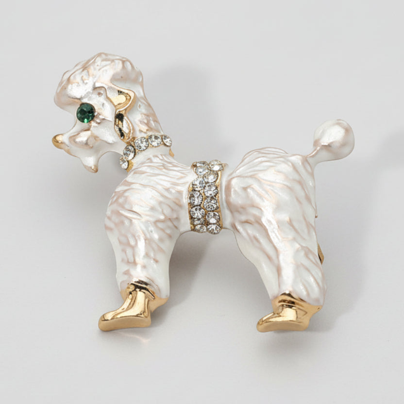 White poodle-shaped brooch with gold and crystal details on a light gray background