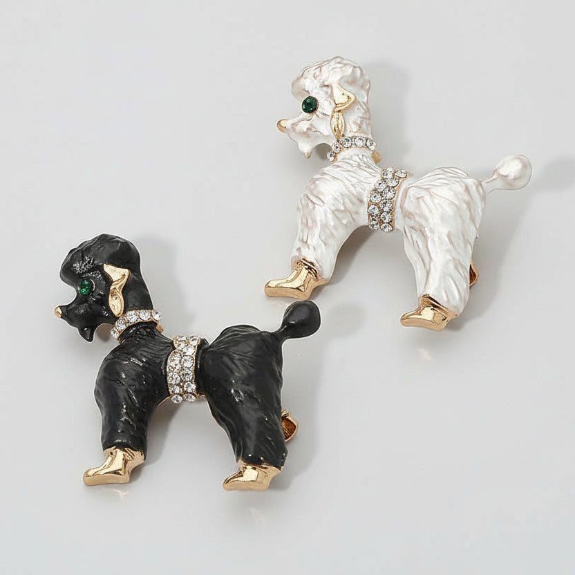 Black and white poodle-shaped brooches with gold and crystal details on a light gray background